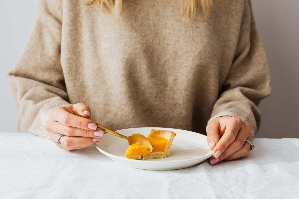 woman in gray sweater holding spoon with sliced orange fruit